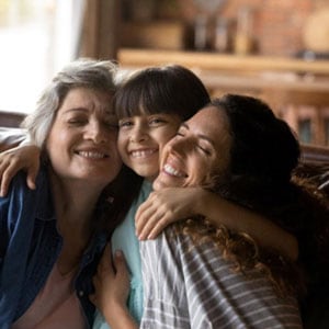 Two women with a small girl smile warmly as they hug each symbolizing Relative Or Kinship Adoptions in Kentucky