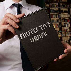 A person in a tie holds a notebook labeled PROTECTIVE ORDER